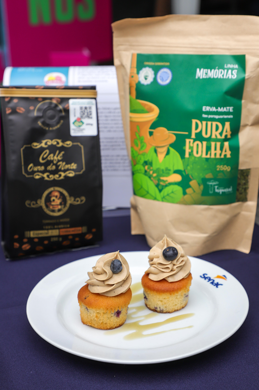 Dois pequenos bolos decorados ao lado de embalagens de café e erva-mate.