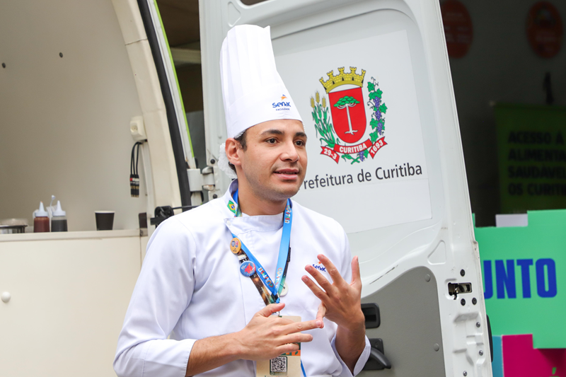 Chef de uniforme branco apresenta uma atividade junto à Cozinha Móvel.