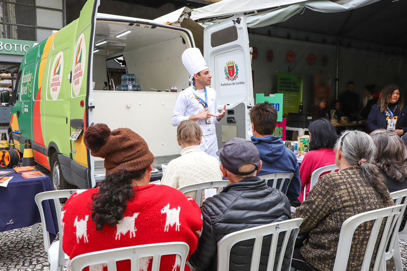 Chef conversa com o público sentado diante da Cozinha Móvel da Prefeitura.