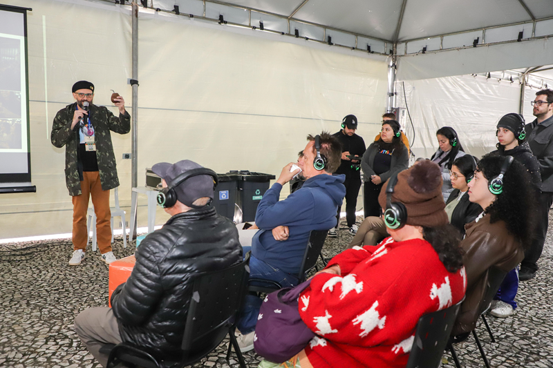Público participa de uma atividade com degustação e fones de ouvido na tenda.